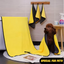 Dog draped in a yellow towel with black borders, towels hanging on a rack, and pet care products in the background.
