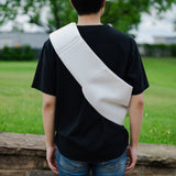 Person wearing a black t-shirt with a white bag slung over one shoulder in an outdoor setting.