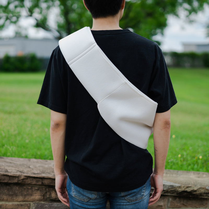 Person wearing a black t-shirt with a white bag slung over one shoulder in an outdoor setting.