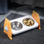 Pet food and water bowls on a raised platform with orange stands on a carpeted floor.