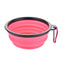 Pink collapsible dog bowl with black rim and carabiner on a white background