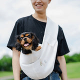 Person holding a small dog in a white sling outdoors