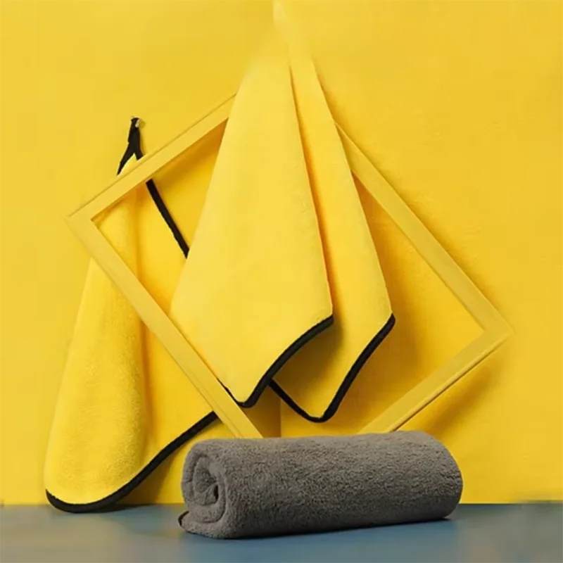 Yellow towel with black trim draped over a geometric frame, with a gray towel rolled up on a blue surface.