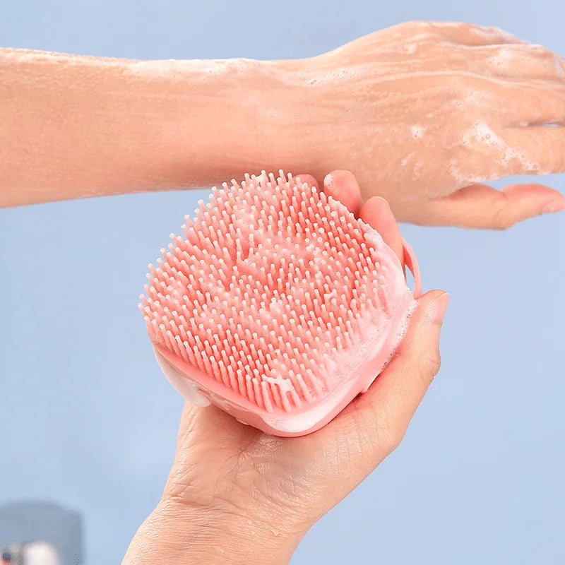 Person using a pink silicone scrubber on their hand against a light blue background